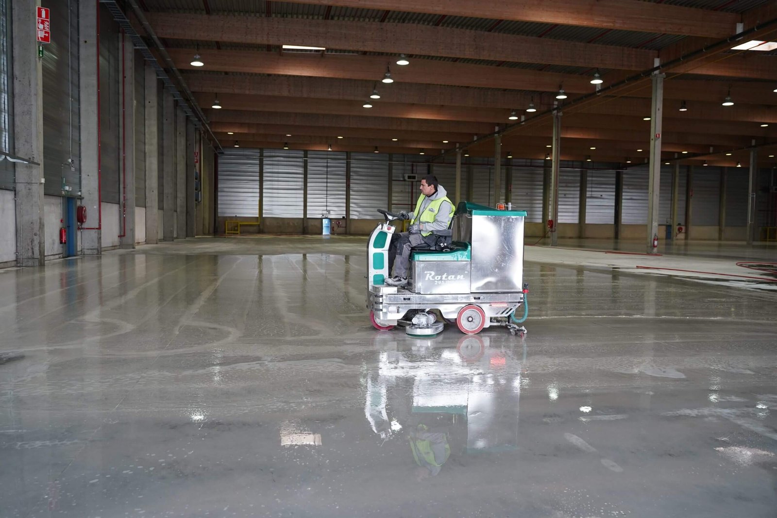 Operario limpiando suelo de almacén grande con máquina.