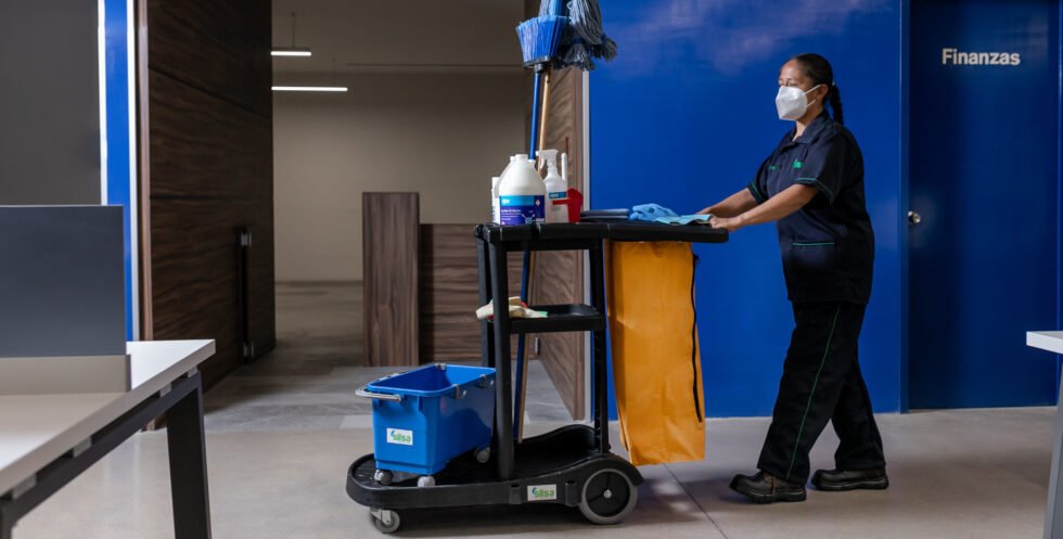 Persona limpiando oficina con carro de limpieza, puerta Finanzas.
